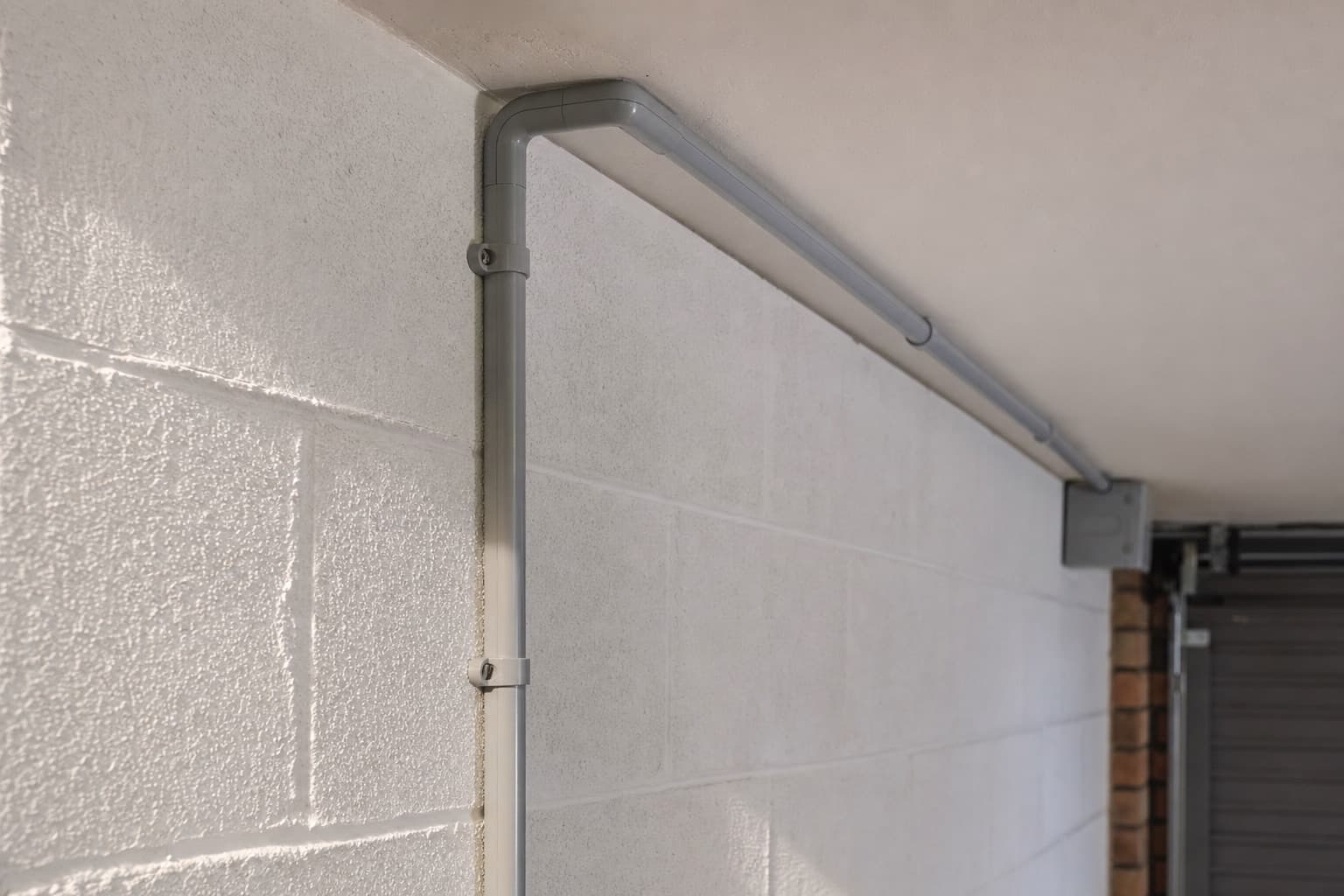 Une goulotte grise qui longe un mur de garage et coude à l’angle du plafond